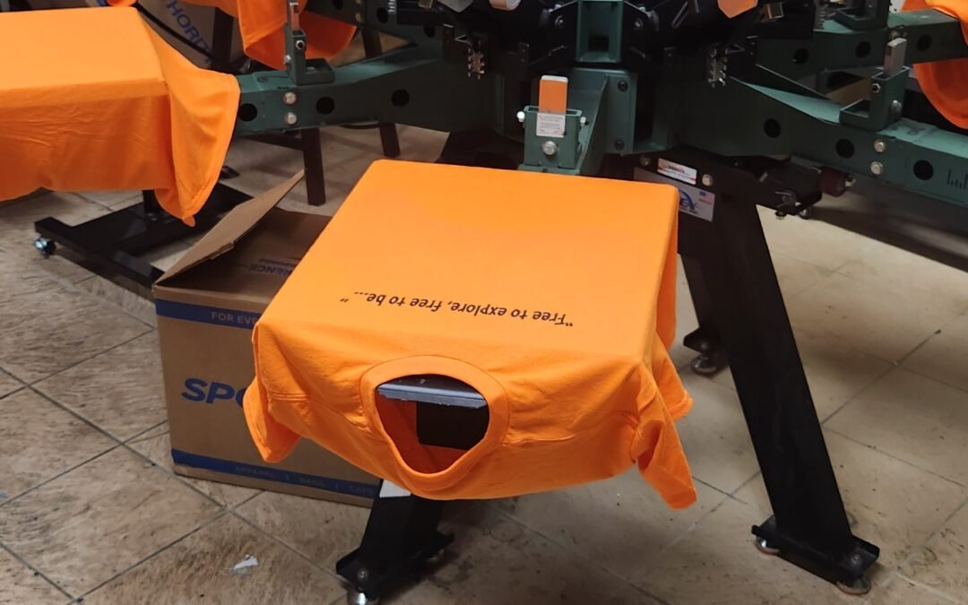 Orange shirts on the screen printing press at Endless Ink Printing